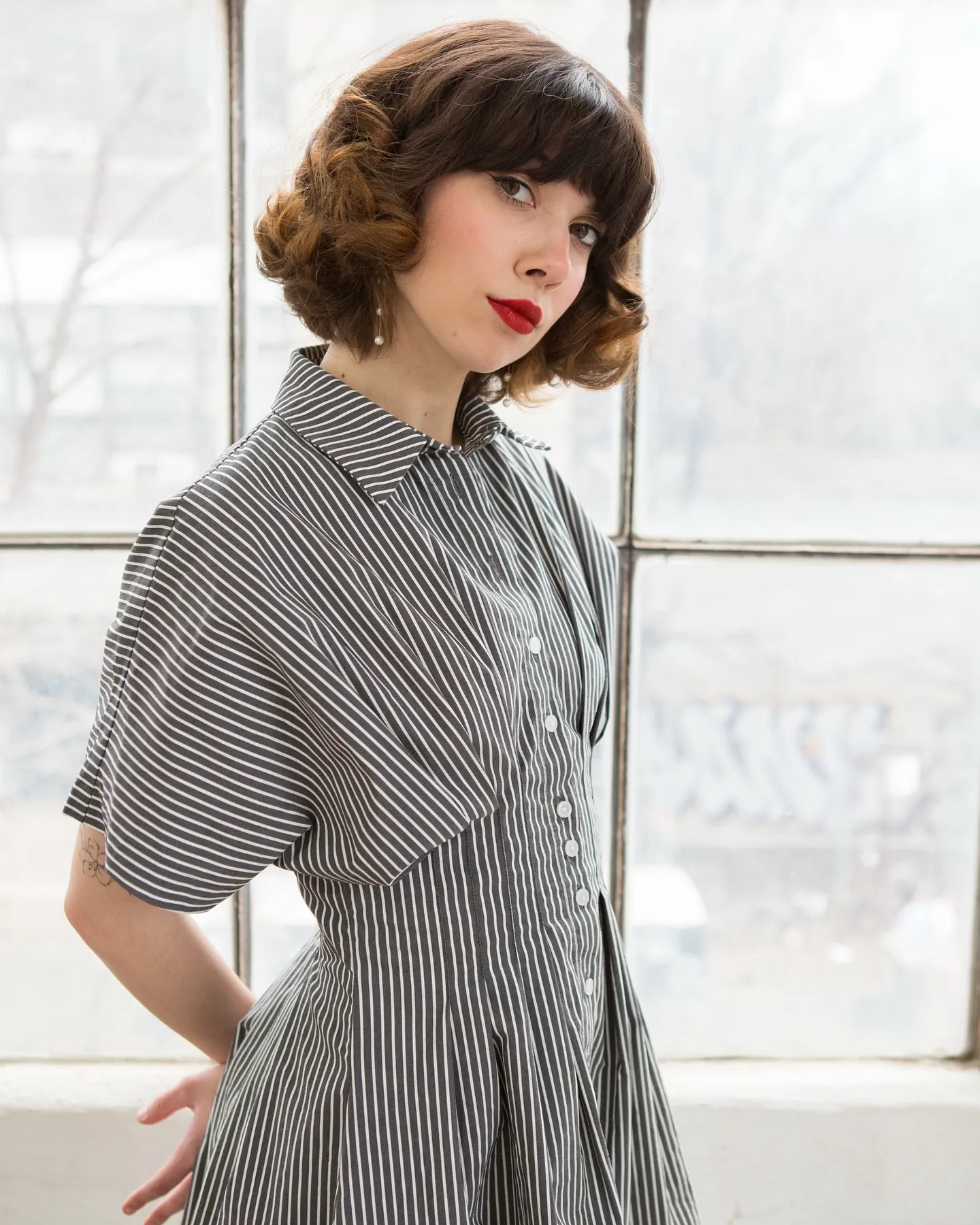 Angie Pastor in a striped shirtdress by a factory window